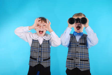 Schoolboy and schoolgirl playing with binoculars. Photos on a blue backgroundの写真素材