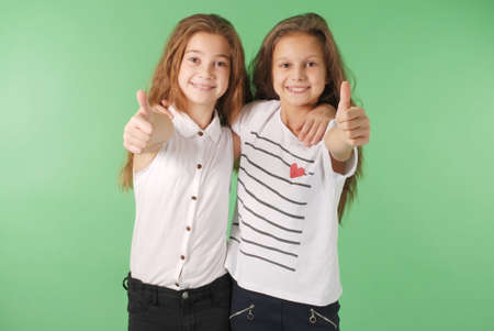 Two smiling young school girls showing thumbs up isolated on green backgroundの写真素材