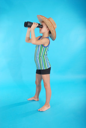 Curious boy in cowboy hat looking through binoculars. Photo on a blue background