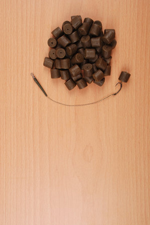 Fishing bait with hook and brown pre-drilled halibut pellets for carp fishing isolated on wood background with soft shadowの写真素材