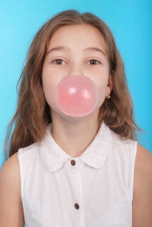Girl blowing a big bubble gum bubble isolated on blueの写真素材
