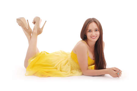 Beautiful woman with brown hair in elegant yellow dress lying on white backgroundの写真素材