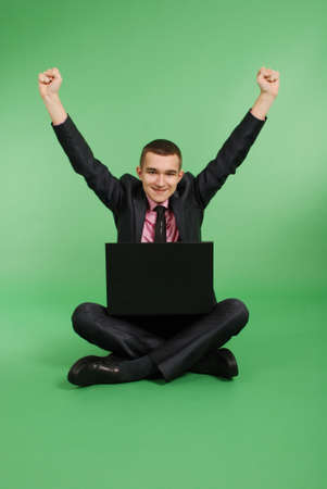 Full length portrait of confident mature businessman which working in laptop in formals sitting isolated over green backgroundの写真素材