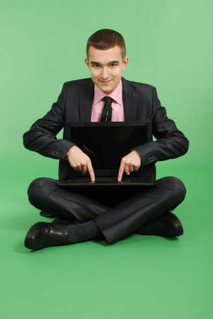 Full length portrait of confident mature businessman which working in laptop in formals sitting isolated over green backgroundの写真素材