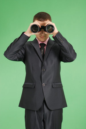 Full length portrait of confident young businessman which looks through binoculars in formals standing isolated over green backgroundの写真素材