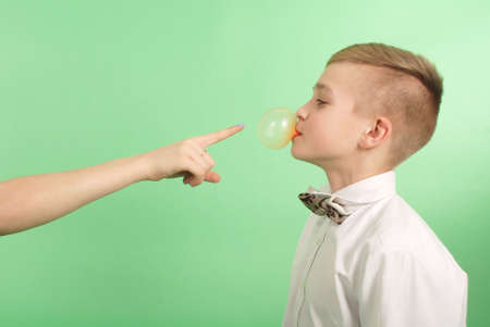 Young boy stretching from chewing gum which he carries in his mouth isolated on green backgroundの写真素材