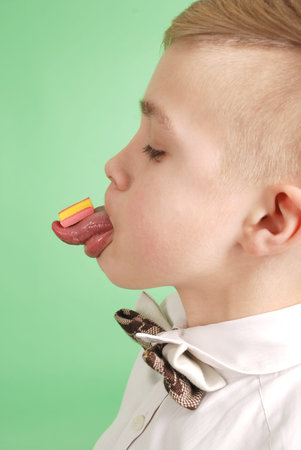 Young boy put the chewing gum on his tongue isolated on green background