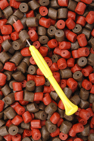 Yellow stinger needle and brown with red pre-drilled halibut pellets for carp fishing  background