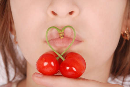 close-up portrait of beautiful girl's lower part of face with two red cherries fruits with heart shaped stemの写真素材