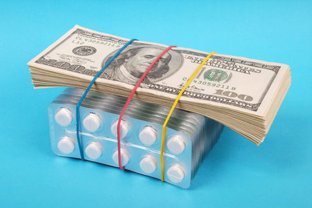 Pack of dollars lays on packing of white tablets. On blue background.