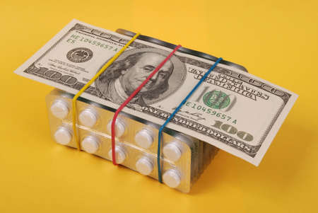 Hundred dollars lays on packing of white tablets. On yellow background.の写真素材