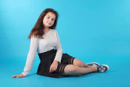 Young girl sitting on floor against blue background in studio.の写真素材