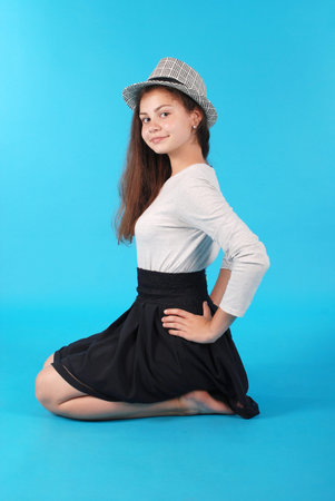 Young girl sitting on floor against blue background in studio.の写真素材