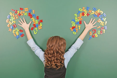 Girl stands in front of a green school board with magnets of numbers on green background