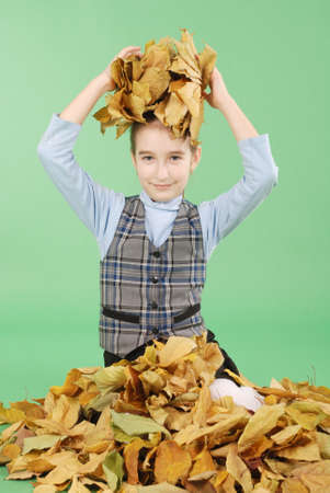 Autumn. Young girl holds autumn yellow leaves. Cute girl in school uniform. Autumn time. Season and autumn holiday.  Isolated on green backgroundの写真素材