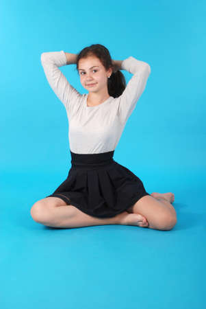 Young girl sitting on floor against blue background in studio.の写真素材