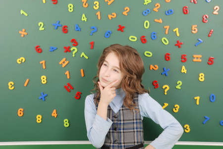 Girl stands in front of a green school board with magnets of numbers that depict her thoughts on green backgroundの写真素材