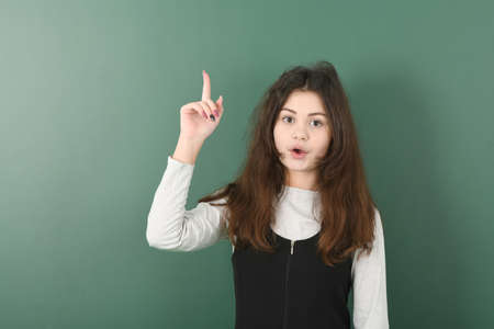 Smiling little schoolgirl shows a finger up green backgroundの写真素材