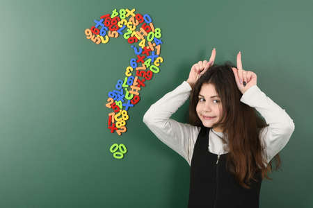 Smiling little schoolgirl on green school board. On the part of her head there is a sign of the question of magnetic lettersの写真素材