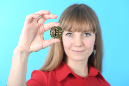 Pretty Girl holding new golden cryptocurrency bitcoin in hands on blue backgroundの写真素材
