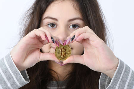 Pretty Girl holding and shows the heart new golden cryptocurrency bitcoin in hands on white backgroundの写真素材