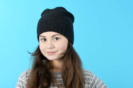Portrait beautiful girl in striped blouse and winter hat, on blue backgroundの写真素材