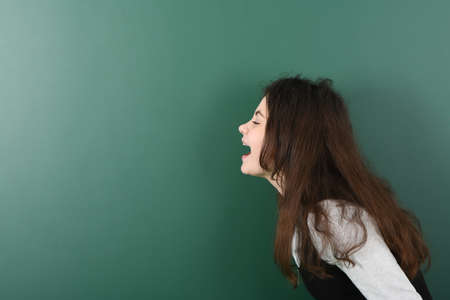 Smiling little schoolgirl on green background . Young playful girl screamsの写真素材