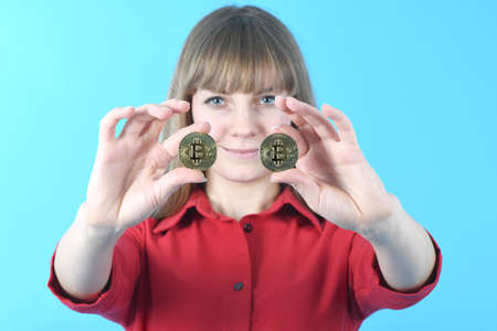 Pretty woman holding new golden cryptocurrency bitcoin in hands on blue backgroundの写真素材