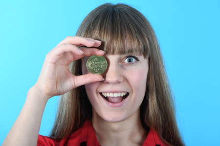 Pretty Girl holding in front of her new golden cryptocurrency bitcoin in hands on blue backgroundの写真素材