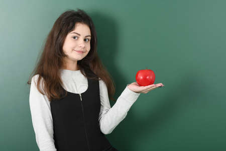 Smiling little schoolgirl on green background . Young playful girl holds an apple in her handの写真素材
