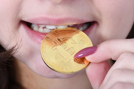 Pretty Girl keeps and trying to taste golden cryptocurrency bitcoin in hands on white backgroundの写真素材