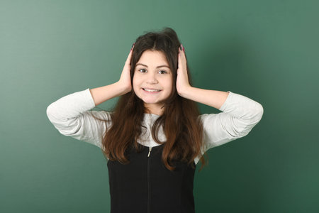 Smiling little schoolgirl on green background . Young playful girl closes her earsの写真素材
