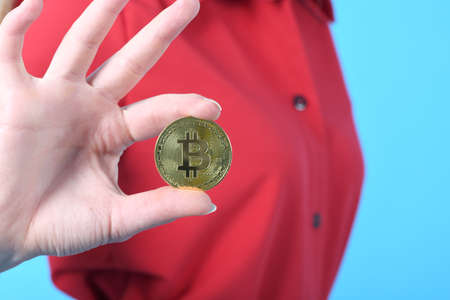 Pretty woman holding new golden cryptocurrency bitcoin in hands on blue backgroundの写真素材