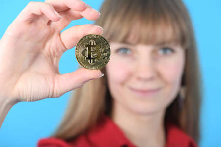 Pretty Girl holding new golden cryptocurrency bitcoin in hands on blue backgroundの写真素材