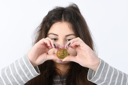 Pretty Girl holding and shows the heart new golden cryptocurrency bitcoin in hands on white...