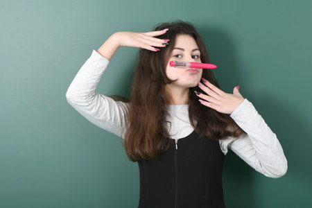 Smiling little schoolgirl on green background . Young playful girl making mock moustache using a pen
