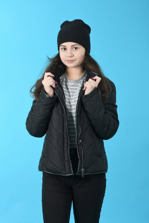 Portrait beautiful girl in winter black jacket and hat, on blue background