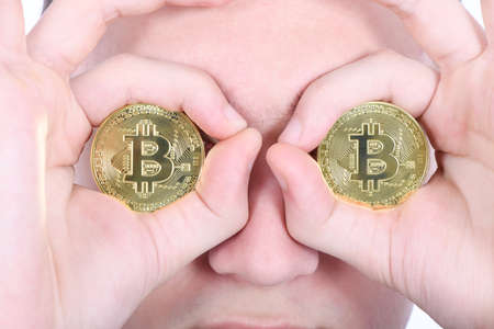 Man keeps the eye instead two golden cryptocurrency bitcoin in hands on white backgroundの写真素材