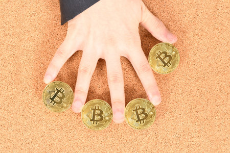 Man's hand holding golden Bitcoin on brown textured cork background. High resolution photo. Full...