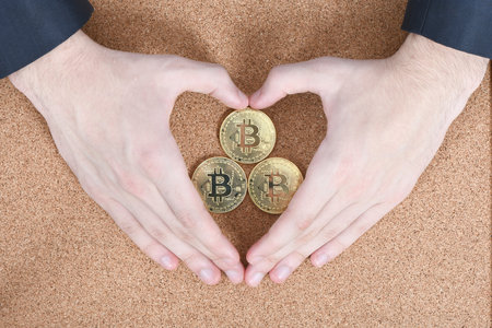 Hands holds and shows the heart new golden cryptocurrency bitcoin on brown textured cork