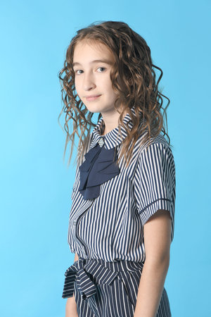 Portrait of adorable smiling schoolgirl with curl hair, standing isolated on a blue background. High...