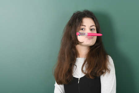 Smiling little schoolgirl on green background . Young playful girl making mock moustache using a penの写真素材