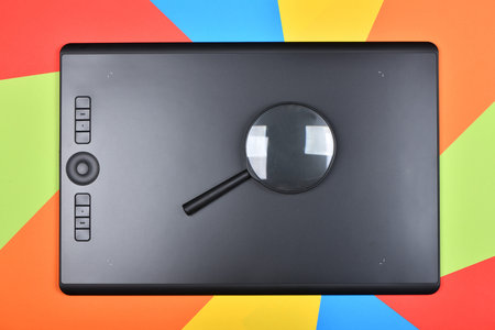 Top view magnifying glass on professional graphics tablet. Isolated on multicolored background. High...