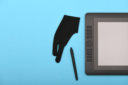 Graphic monitor stylus and glove on blue color table. Black tablet computer with blank screen. High...