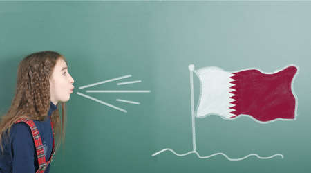 Pre-adolescent girl blowing on the school board drawn on the blackboard Qatar flag. High resolution photo. Full depth of field.の写真素材