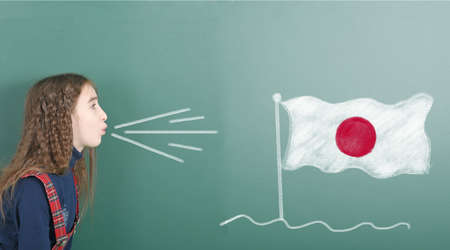 Pre-adolescent girl blowing on the school board drawn on the blackboard Japan flag. High resolution photo. Full depth of field.の写真素材