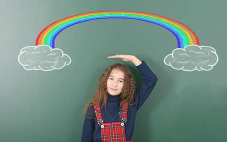 Pre-adolescent girl stands under chalk drawn rainbow. Rainbow emerges from the cloud and disappears after another. High resolution photo. Full depth of field.の写真素材