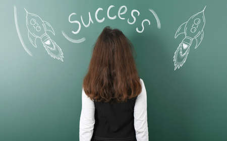 Pre-adolescent girl turns her back and looks at the inscription "success". Inscription and two rockets drawn in chalk. High resolution photo. Full depth of field.の写真素材