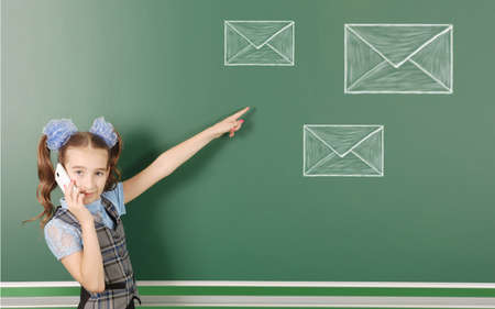 Pre-adolescent girl checks your email, isolated school board background with drawn chalk postcards. High resolution photo. Full depth of field.の写真素材