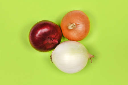 Three onion bulbs of different colors (red, yellow and white) isolated on green background. High resolution photo. Full depth of field.の写真素材